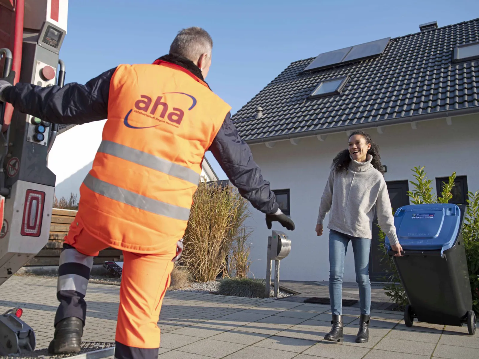 Müllwerker von aha nimmt eine Altpapiertonne von einer Kundin entgegen.